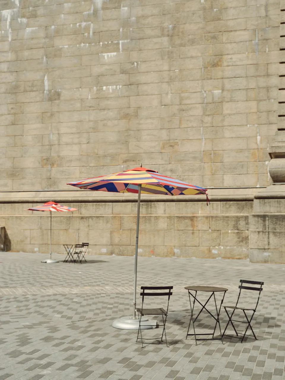 Striped parasols and chairs against a pale stone wall.